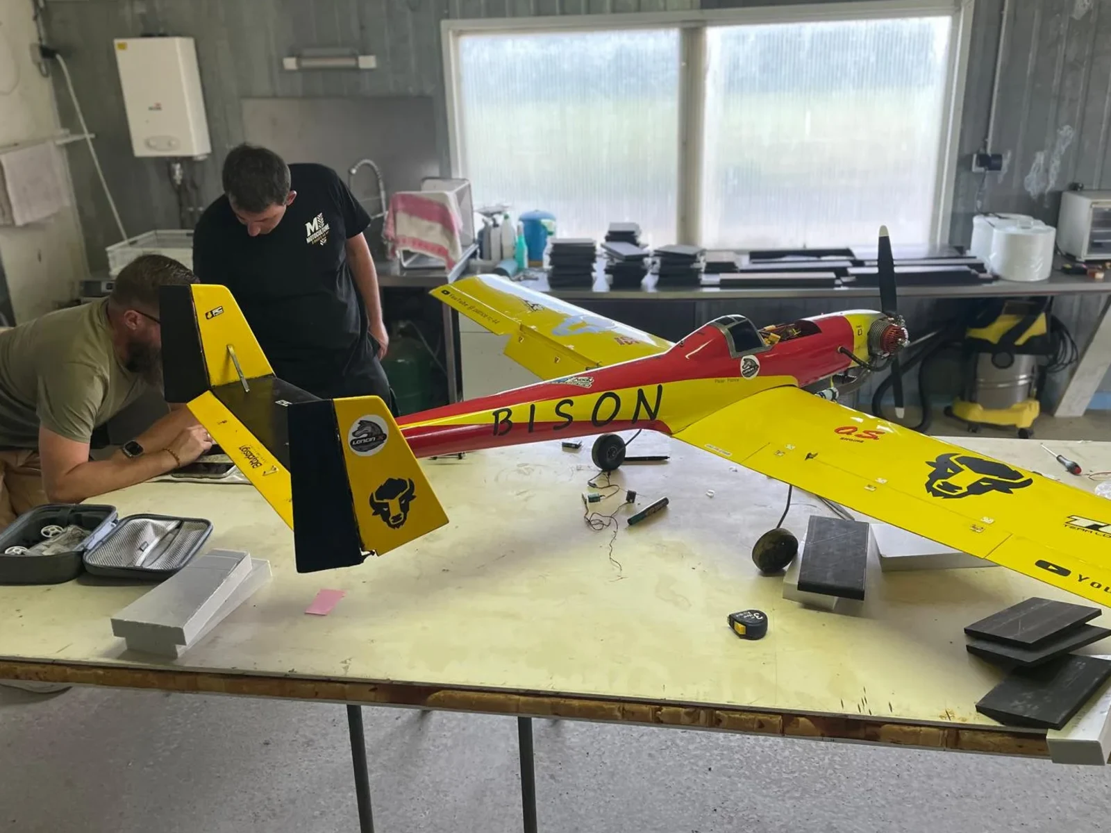 Grand avion radiocommandé Bison rouge et jaune assemblé sur une table d’atelier pendant sa remise en état.