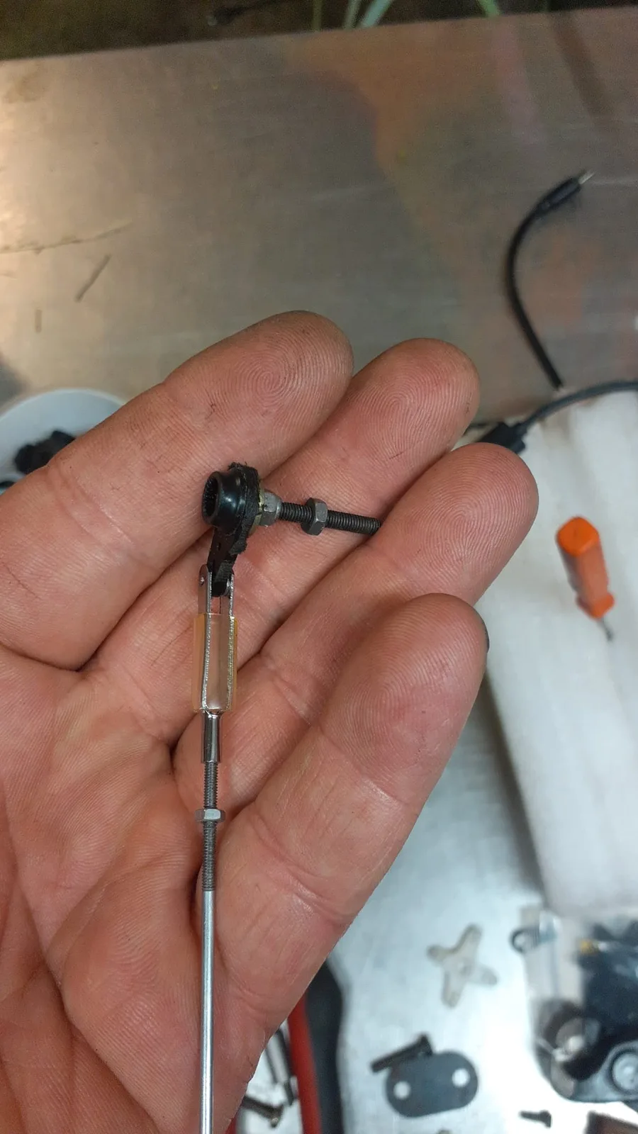 Gros plan sur une tringlerie et une chape de commande tenues dans la main.